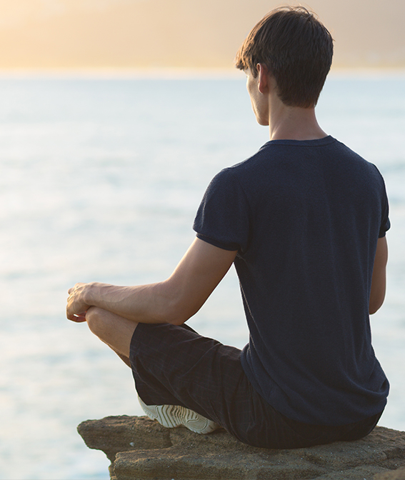 A man sitting on a rock by the water at golden hour
